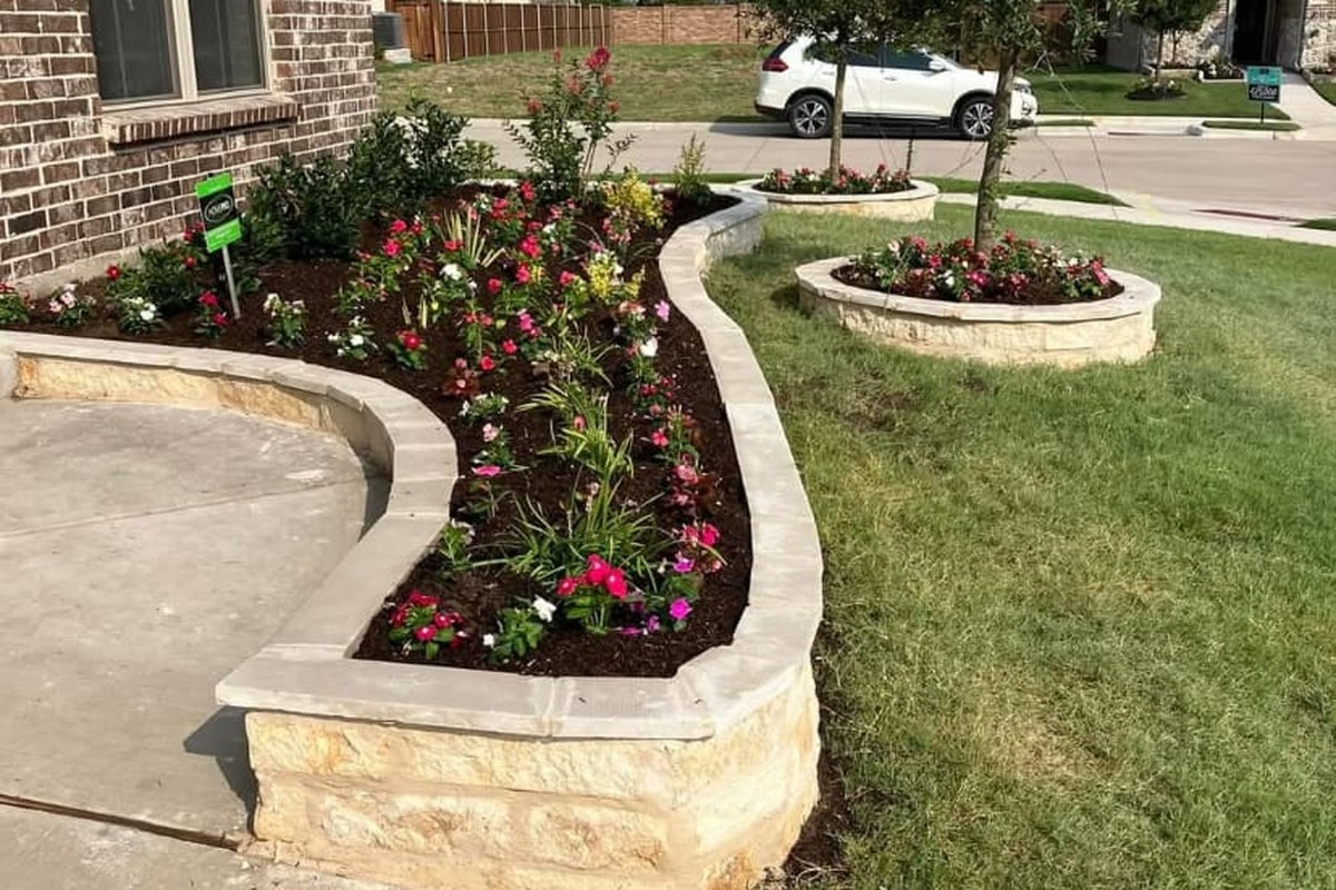 Jardín frontal con jardineras de piedra y flores